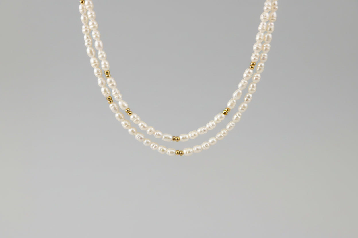 Two-layered pearl necklace with gold beads on a gray background