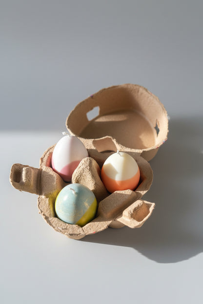 Candle in  an egg carton with three candles inside on a gray surface.