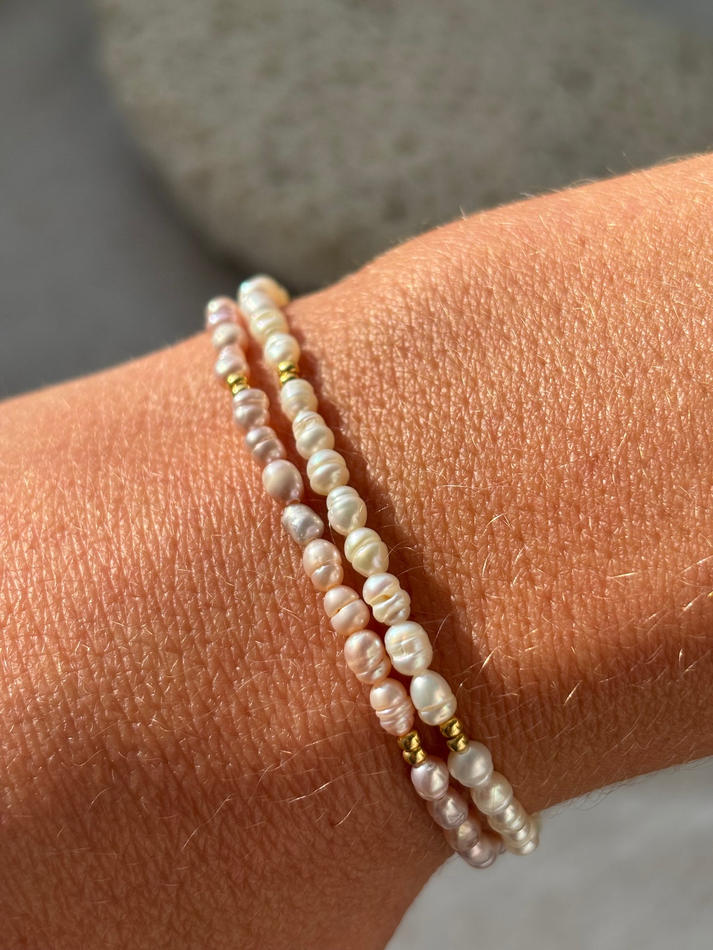 Two pearl bracelets on a wrist with a neutral background