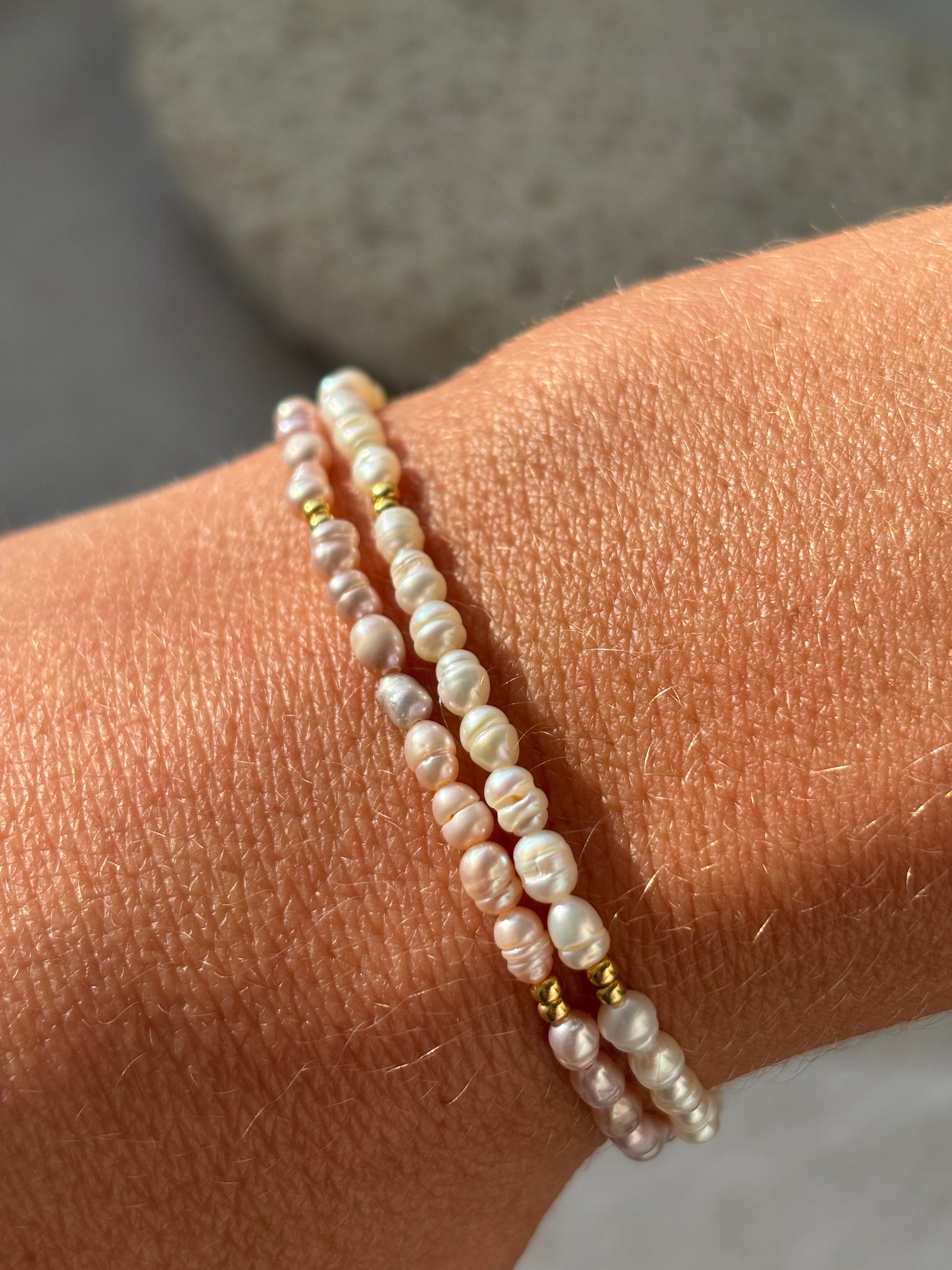 Two pearl bracelets on a wrist with a neutral background