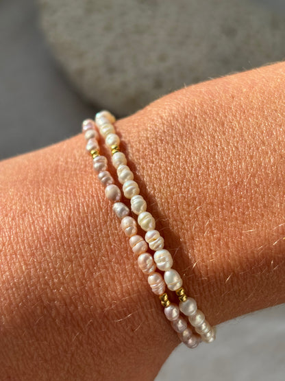 Two pearl bracelets on a wrist with a neutral background