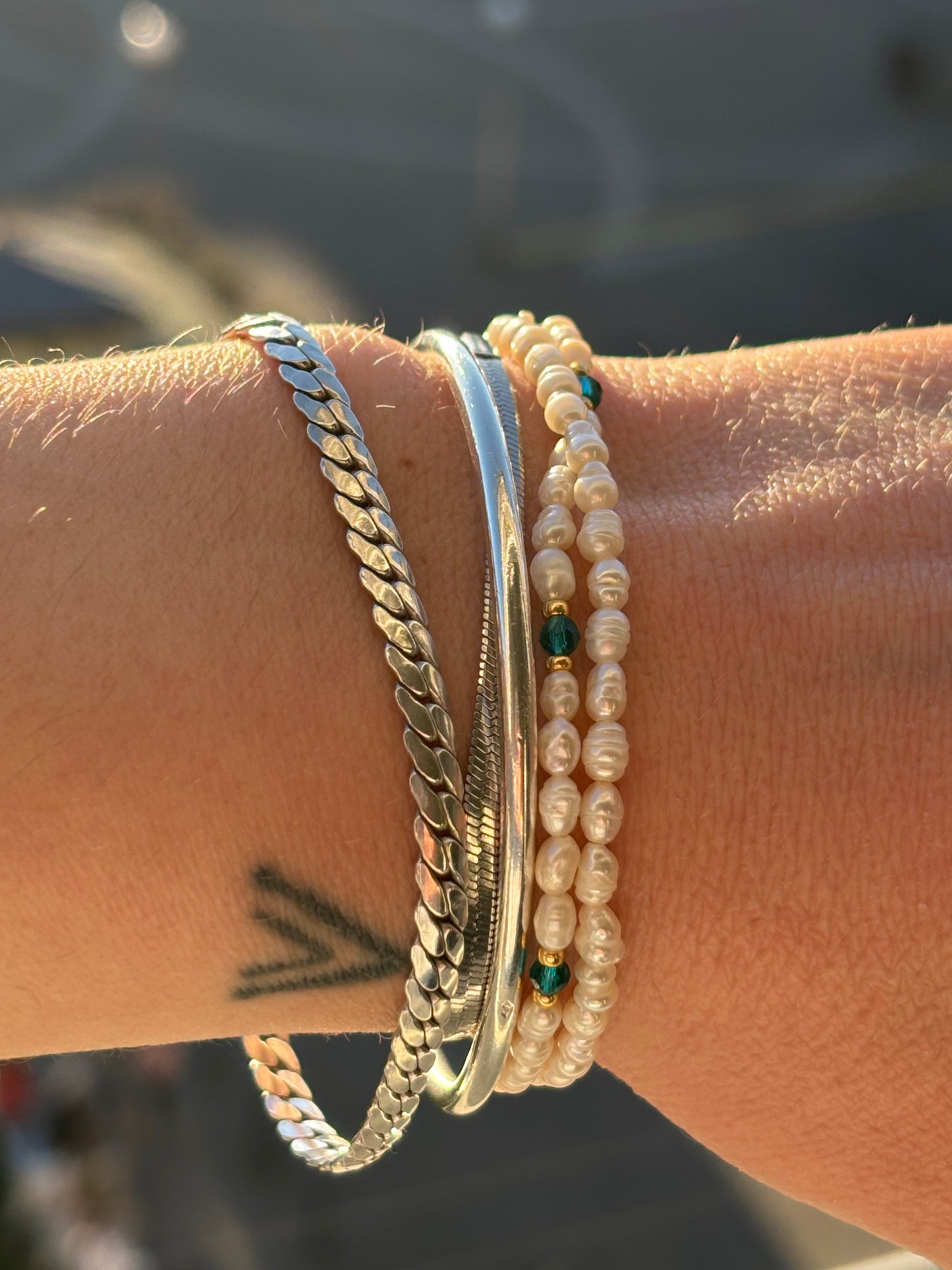 Wrist with multiple bracelets including pearls and chains against a blurred background
