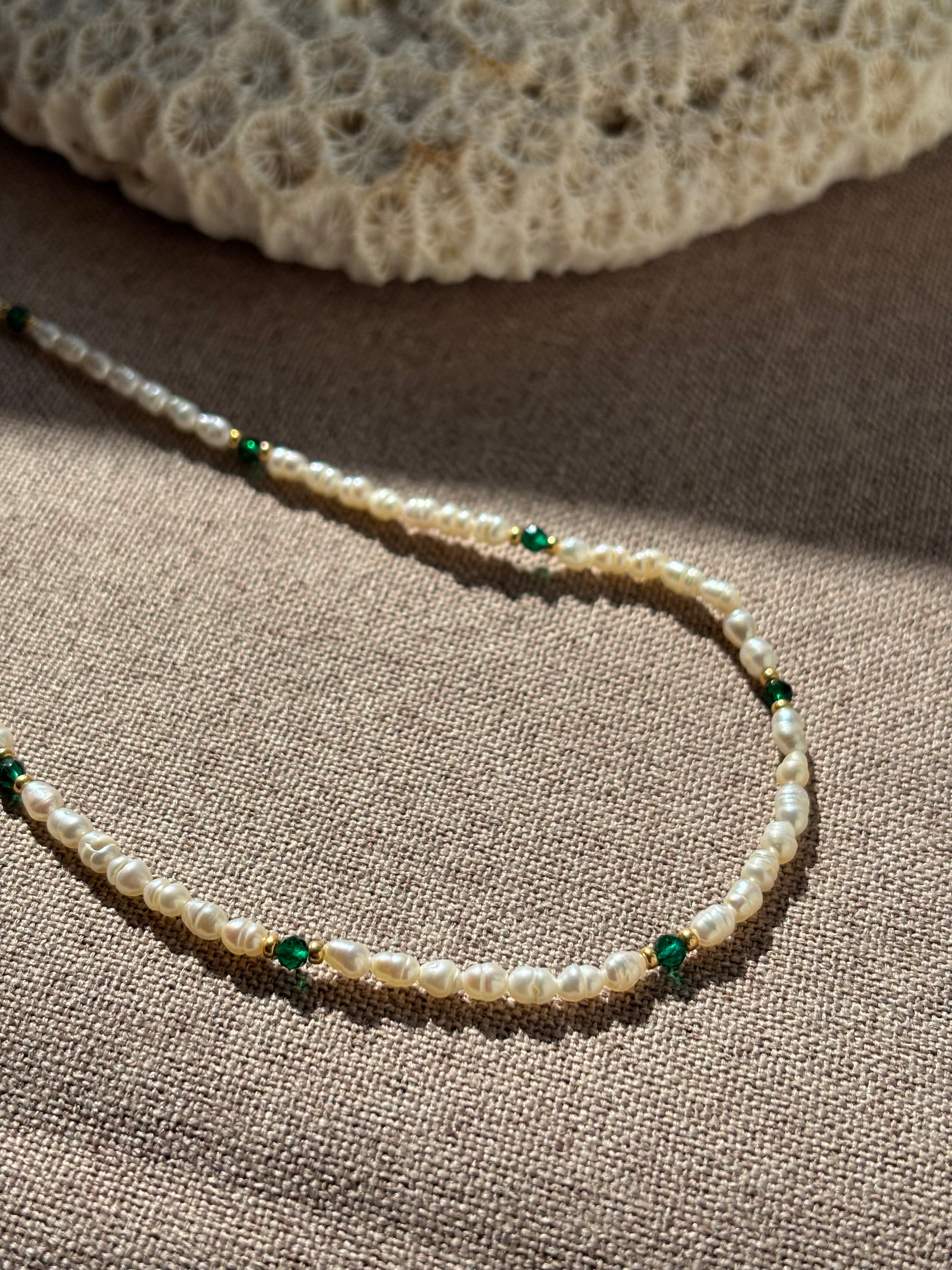 Pearl necklace with green beads on a textured surface