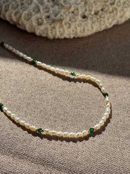 Pearl necklace with green beads on a textured surface