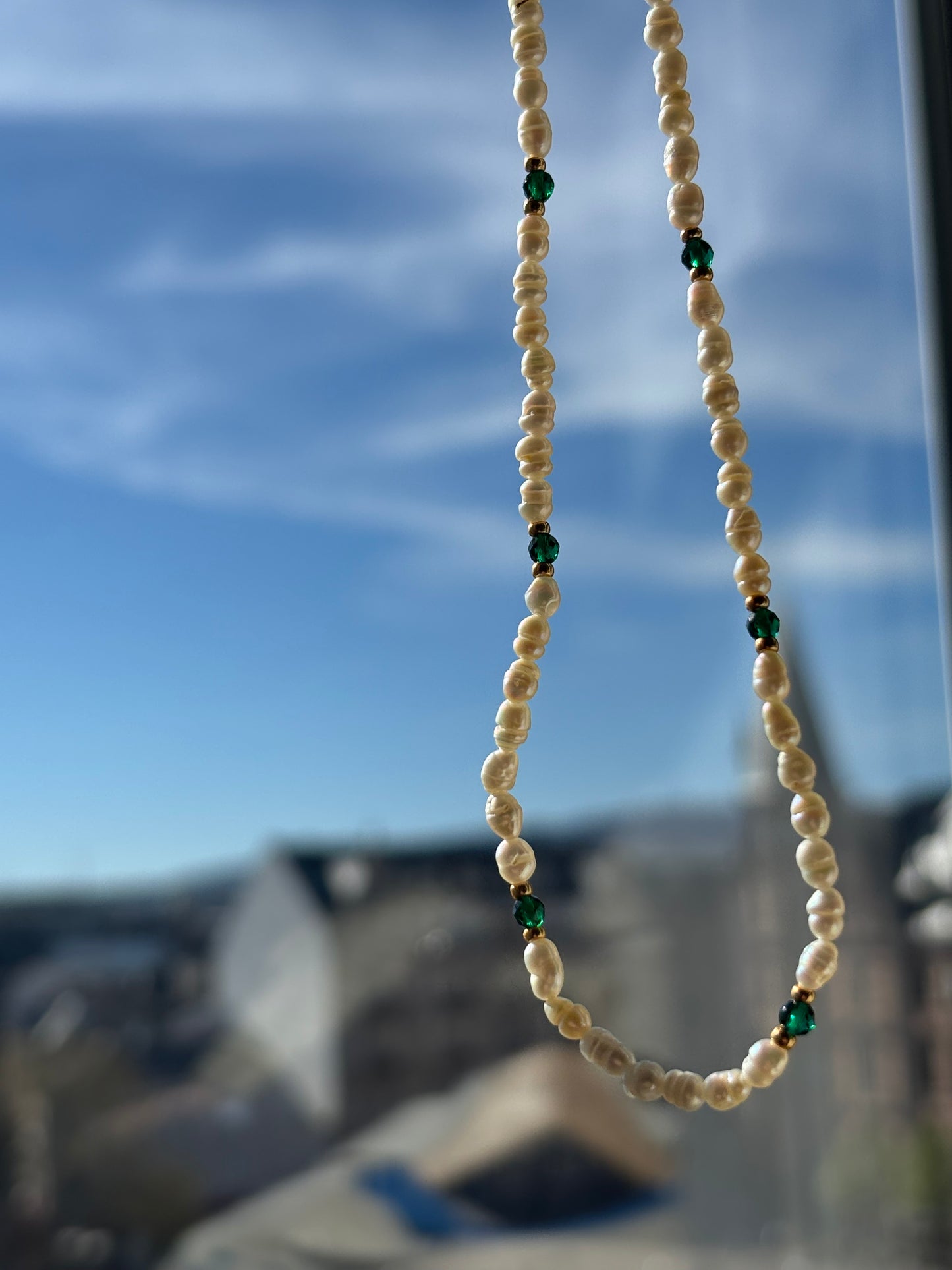 Pearl necklace with green beads against a blurred blue sky background
