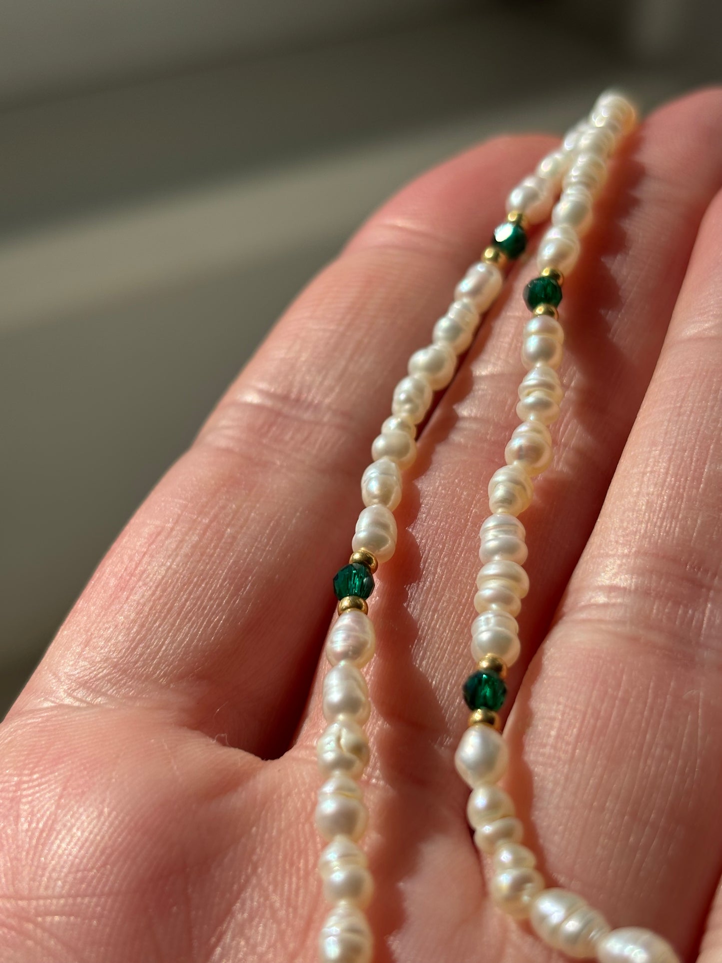 Pearl necklace with green beads held in a hand against a neutral background