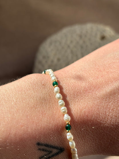 Close-up of a wrist wearing a bracelet with pearls and green beads against a blurred background.