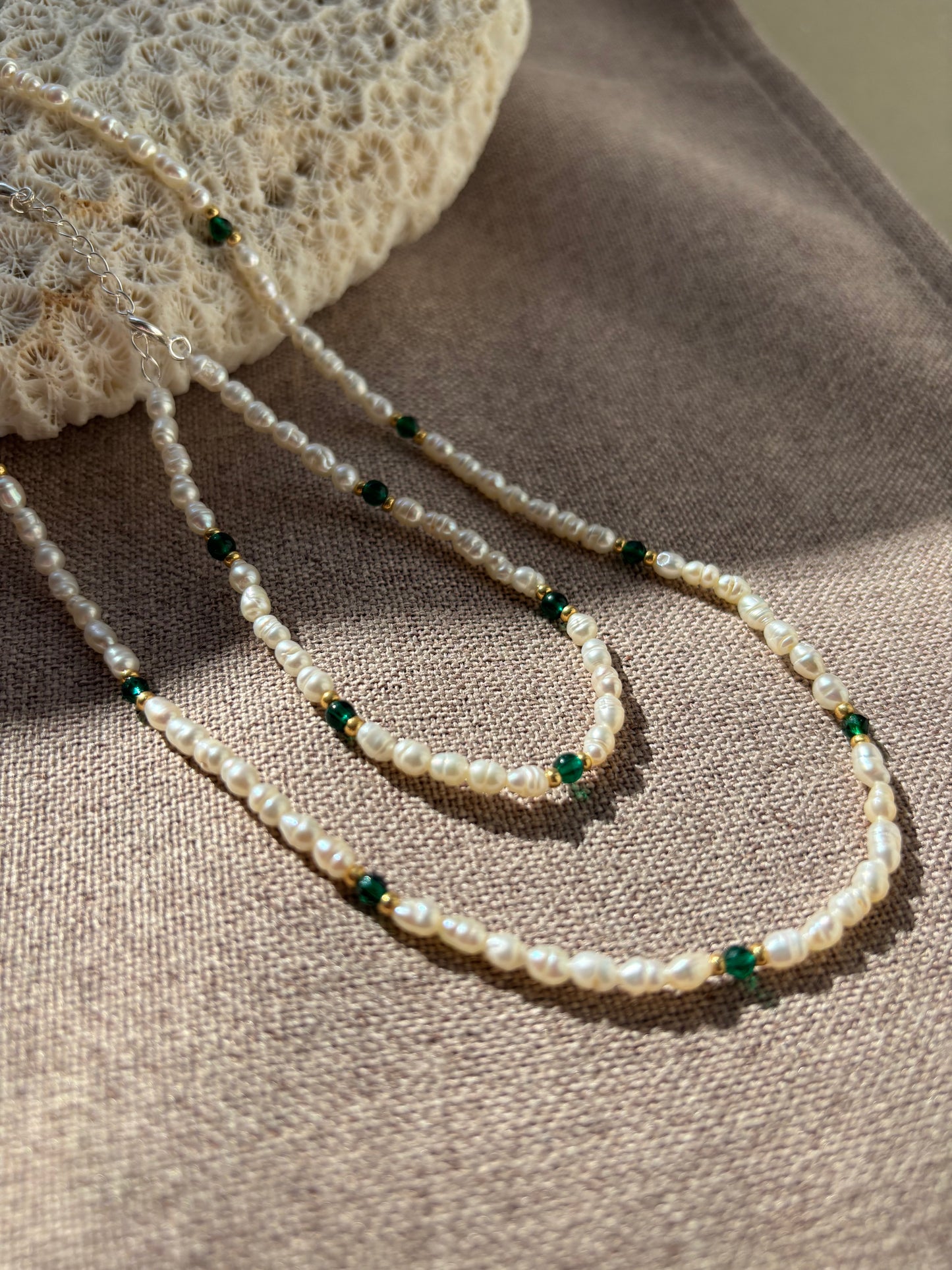 Pearl necklace with green beads on a textured surface