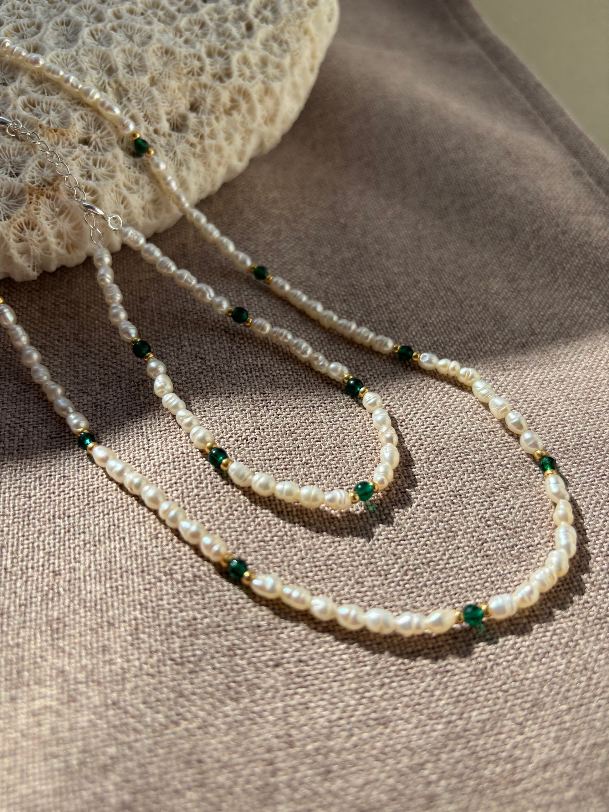 Pearl necklace with green beads on a textured surface