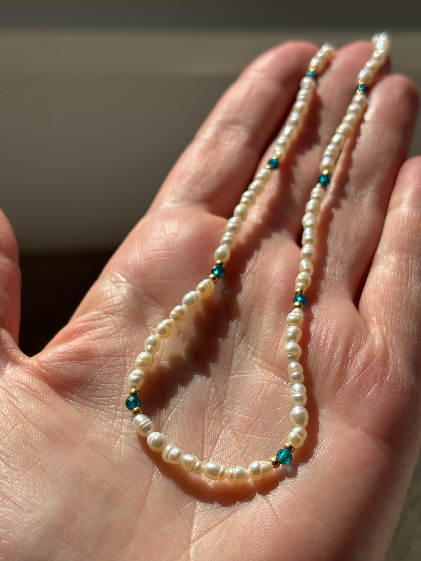 Pearl necklace with blue beads held in a hand against a neutral background