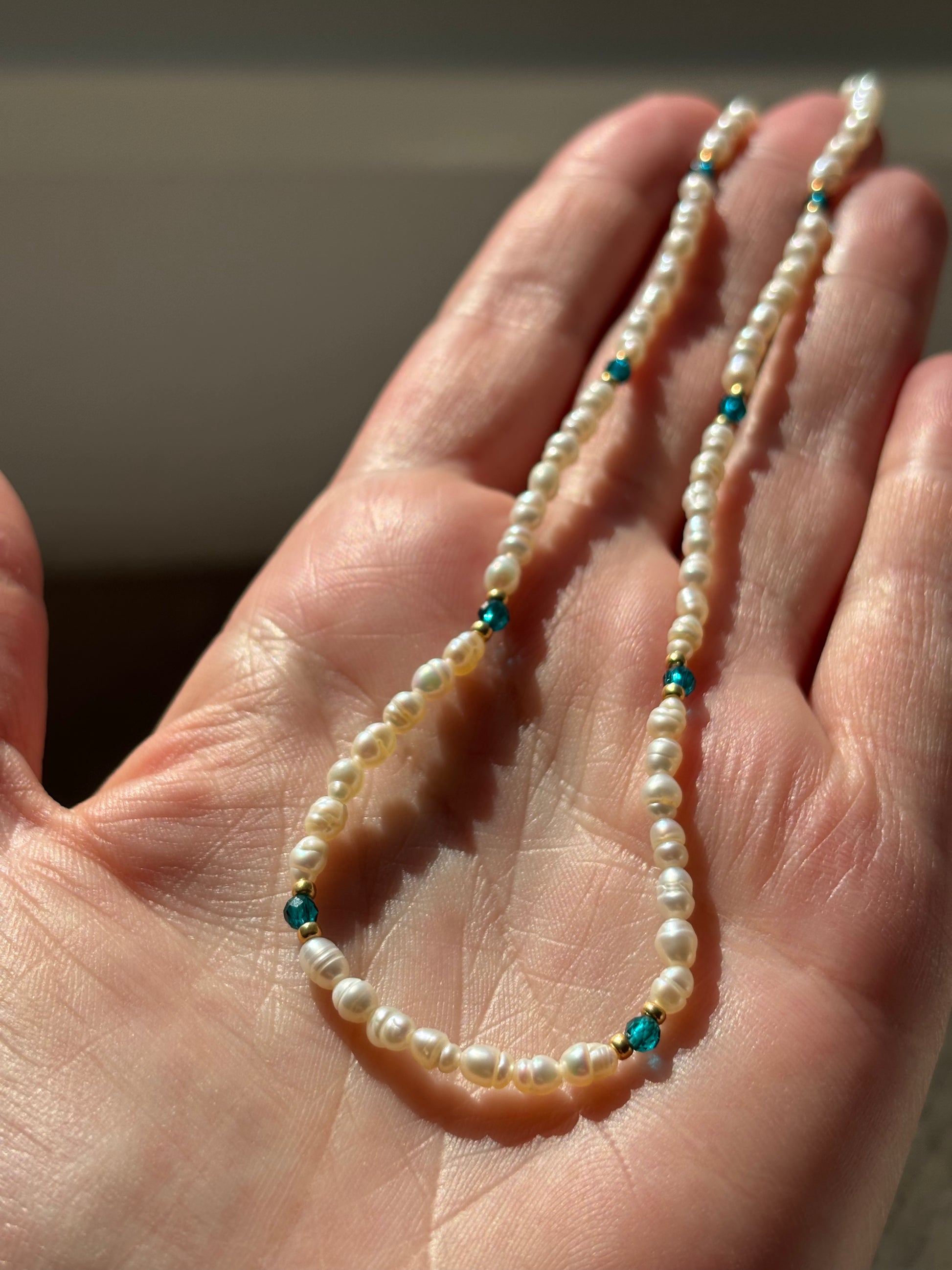 Pearl necklace with blue beads held in a hand against a neutral background