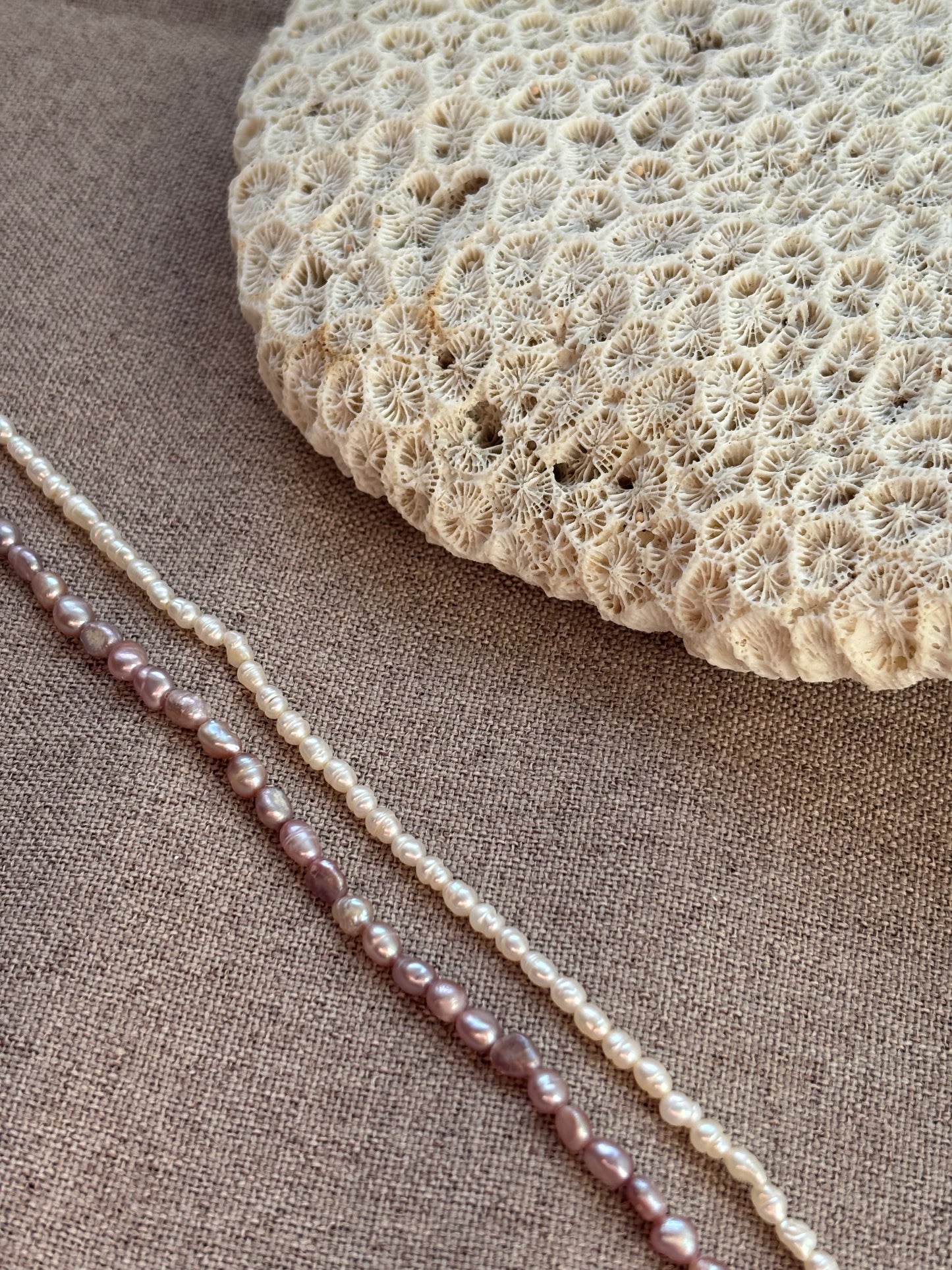 Pearl necklace on a textured fabric surface with a piece of coral.