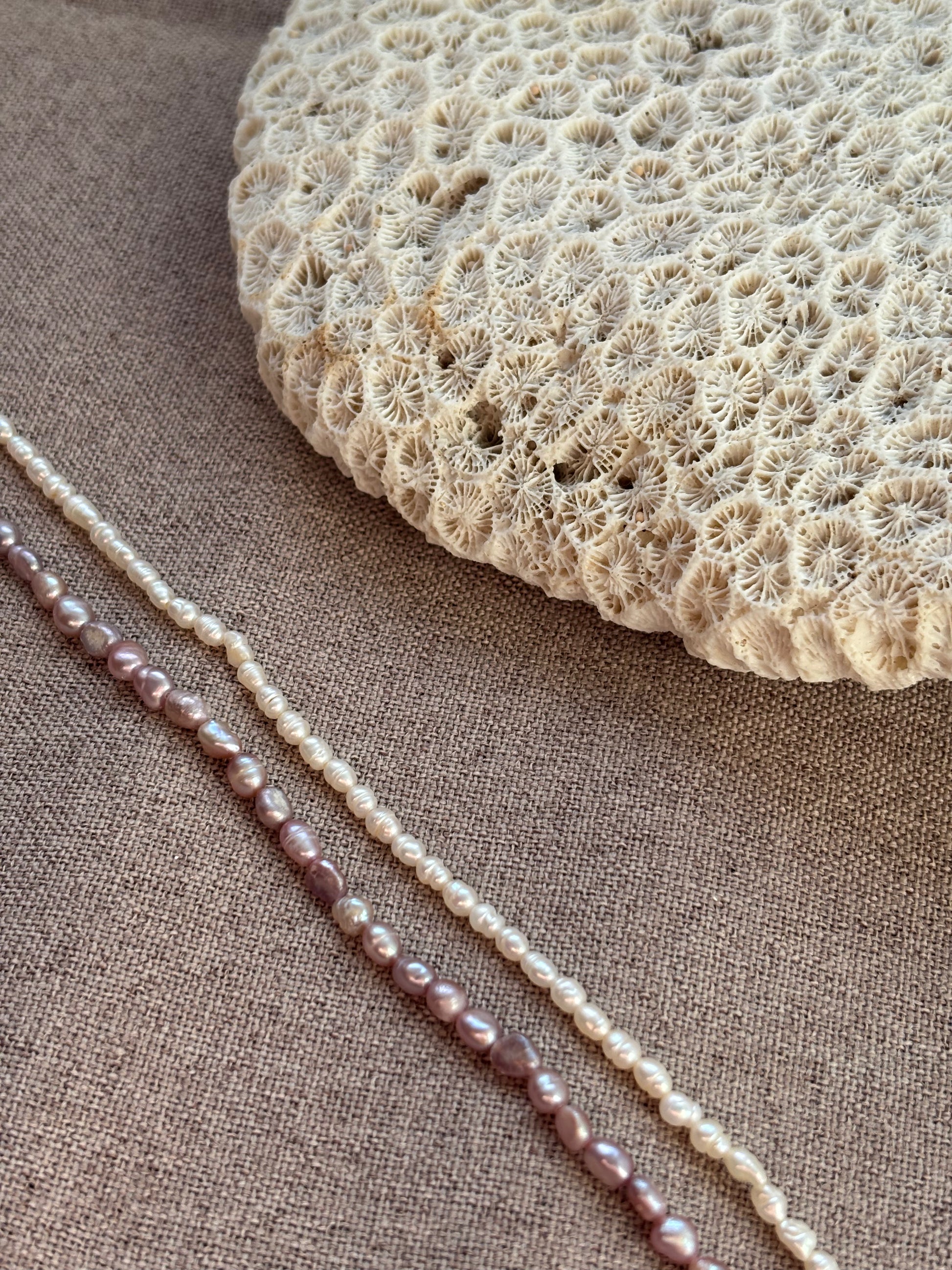 Pearl necklace on a textured fabric surface with a piece of coral.