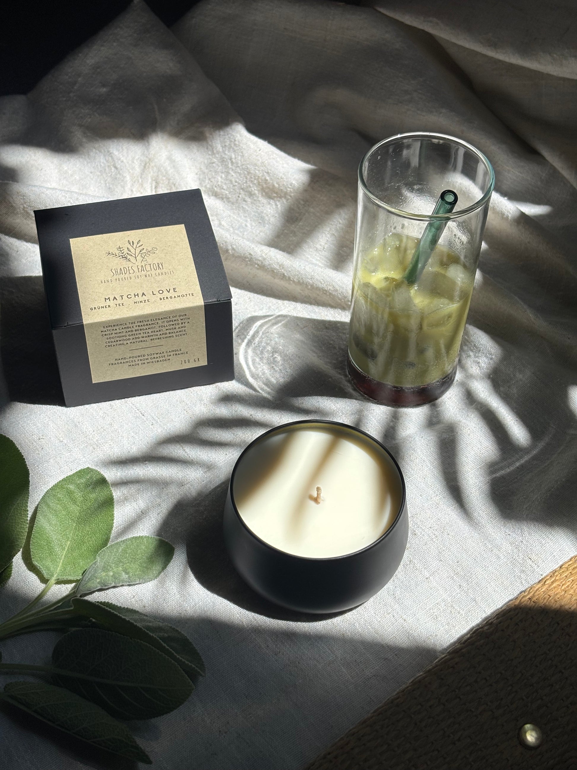 black Candle, glass with a straw, and packaging on a textured surface with green leaves.