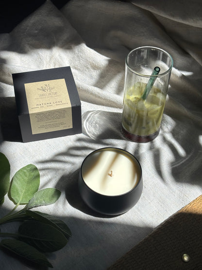 black Candle, glass with a straw, and packaging on a textured surface with green leaves.